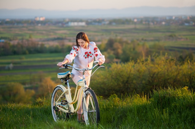 Femme avec vélo rétro sur la colline le soir