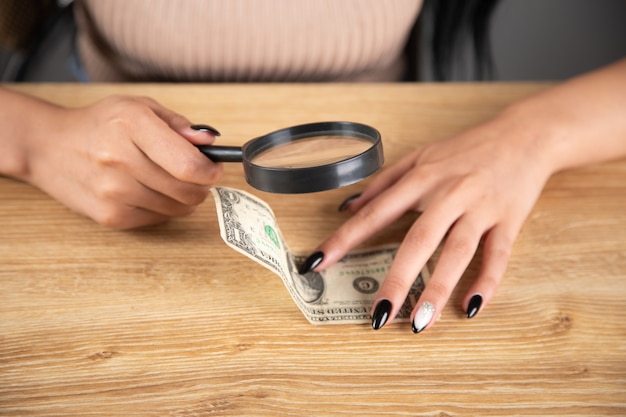 Femme vérifiant un billet d'un dollar avec une loupe