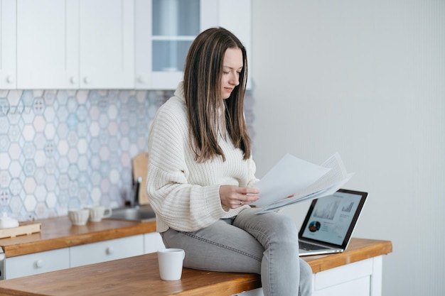 Femme vérifiant des documents financiers dans sa cuisine