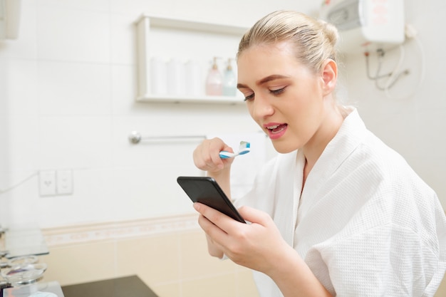 Femme vérifiant le téléphone et se brosser les dents