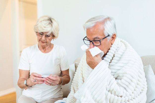 Femme vérifiant la température de la fièvre de l'homme senior assis sur le lit.