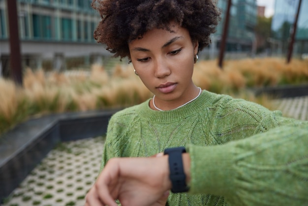 Photo une femme vérifie l'heure de la montre a des moniteurs de rendez-vous distance parcourue sur une montre intelligente après avoir marché en ville porte des poses de cavalier vert décontractées à l'extérieur