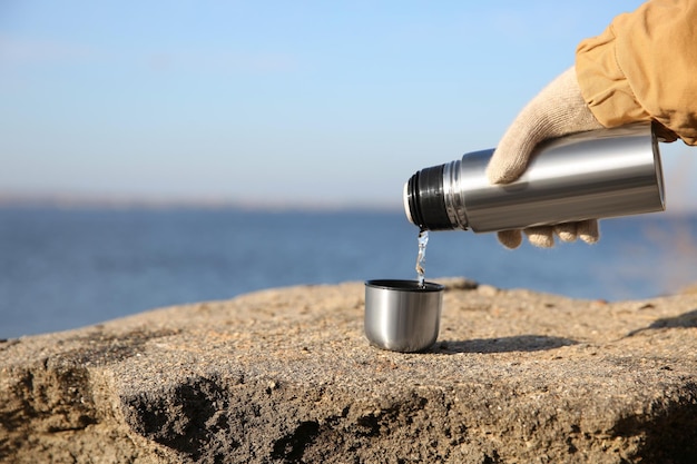 Femme versant une boisson chaude d'une bouteille thermos dans une tasse à l'extérieur en gros plan