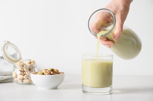 Femme versant du lait de pistache dans du verre sur fond de cuisine blanc Lait végétalien sans lactose à base de plantes