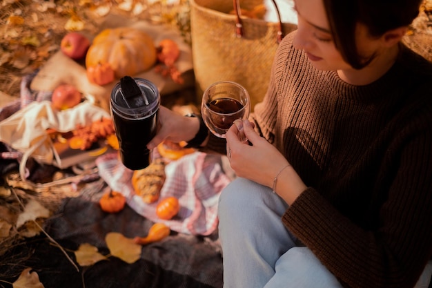 Femme versant du thé à partir d'un thermos dans une tasse se détendre dans la forêt d'automne assis sur le tronc