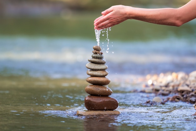 femme versant de l'eau sur des pierres brutes équilibrées comme une pyramide