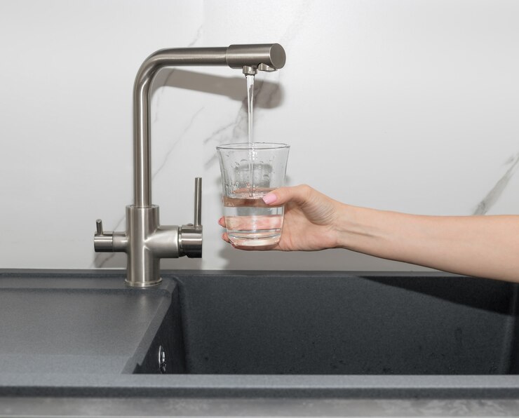 Femme versant de l'eau purifiée filtrée du robinet dans le verre dans l'eau propre de la cuisine
