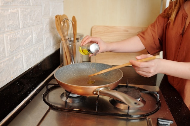 Femme versant de l'huile végétale dans une poêle à frire lors de la cuisson du petit-déjeuner ou du dîner dans la cuisine