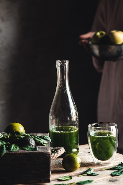 Femme versant un smoothie vert et blanc fraîchement mélangé dans un bocal en verre avec des ingrédients autour d'une table en bois rustique