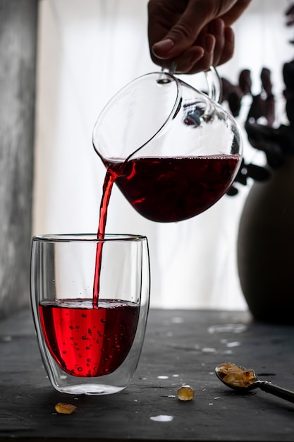 Femme verse du thé d'hibiscus dans un verre