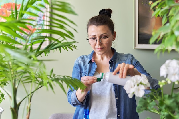 La femme verse de l'engrais minéral liquide. Culture et entretien des plantes d'intérieur en pot. Loisirs et loisirs, jardinage domestique, plante d'intérieur, jungle urbaine en appartement