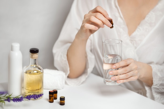 Une femme verse de l'huile aromatique dans un verre d'eau