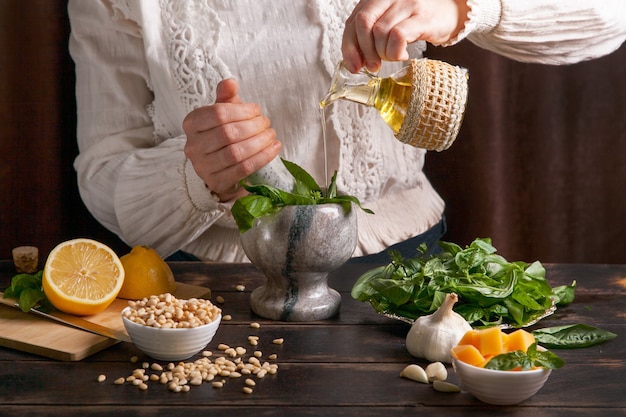 Une Femme Verse De L'huile D'olive Avec Des Feuilles De Basilic Dans Un Mortier Pour Faire Une Saucepesto