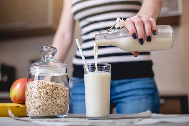 Femme Verse Le Lait D'avoine Biologique D'une Bouteille Dans Un Verre Sur Une Table De La Cuisine. Régime Végétarien Sain