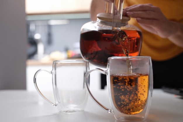 La femme verse le thé de la théière en verre dans le plan rapproché de tasse