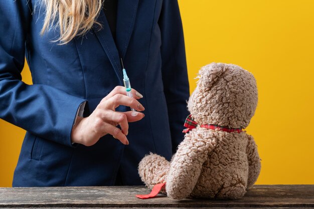 Femme en veste d'affaires tenant une seringue médicale avec un vaccin ou un médicament avec un jouet ours en peluche assis devant elle Image conceptuelle de la pharmacie et de la médecine