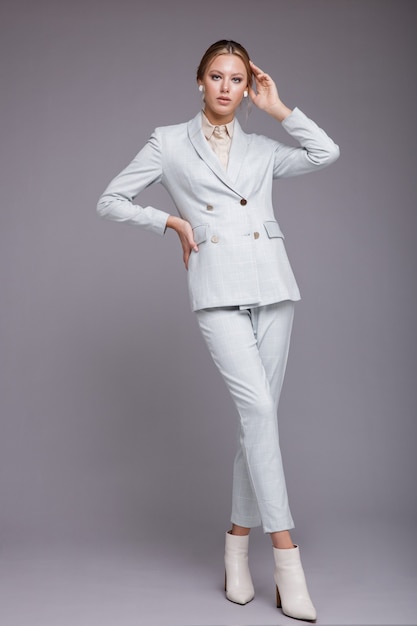 Femme en veste de costume bleu doux pantalon bottes blanches Fond gris Studio shot Couleur monochrome