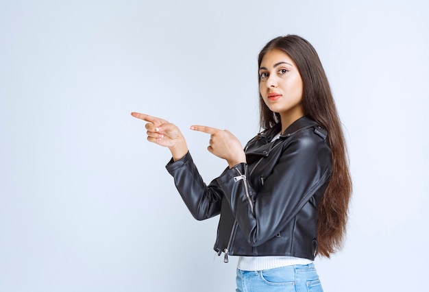 femme en veste de cuir pointant vers quelque chose sur le côté gauche.