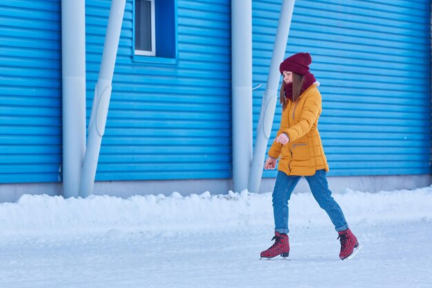 Une femme en veste jaune patine sur le fond d'un bâtiment de sport bleu.