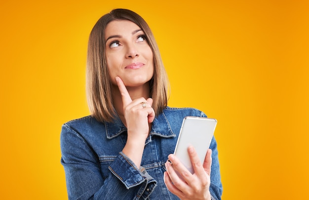 Femme en veste en jean avec smartphone sur fond jaune