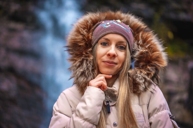 une femme avec une veste marron et un chapeau près d'une cascade