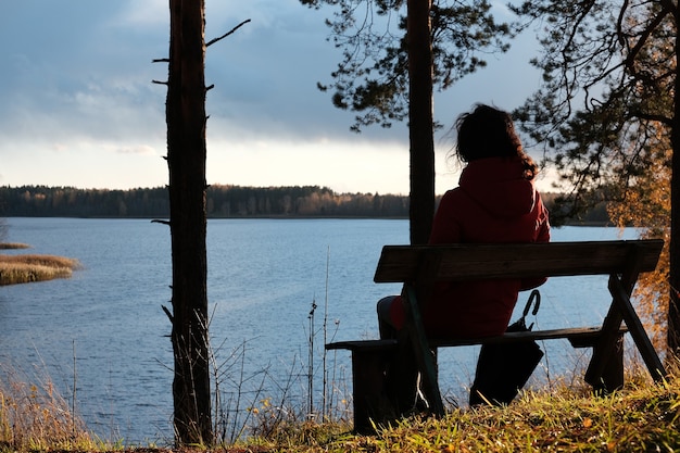 Une femme en veste rouge est assise sur un banc dans le parc