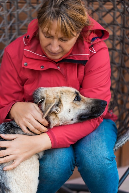 Photo une femme en veste rouge joue et caresse un chien de berger assis sur une chaise en osier