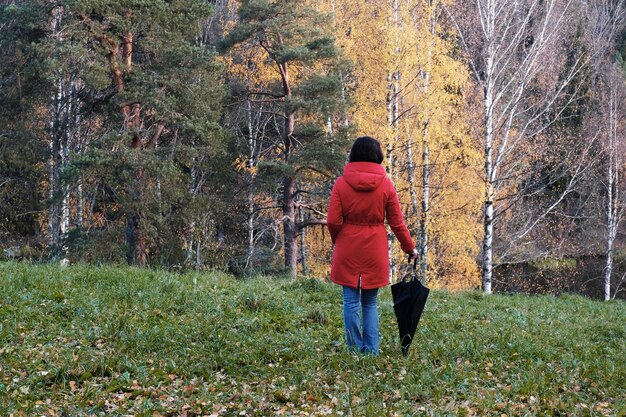 Une femme en veste rouge avec un parapluie se promène dans le parc d'automne
