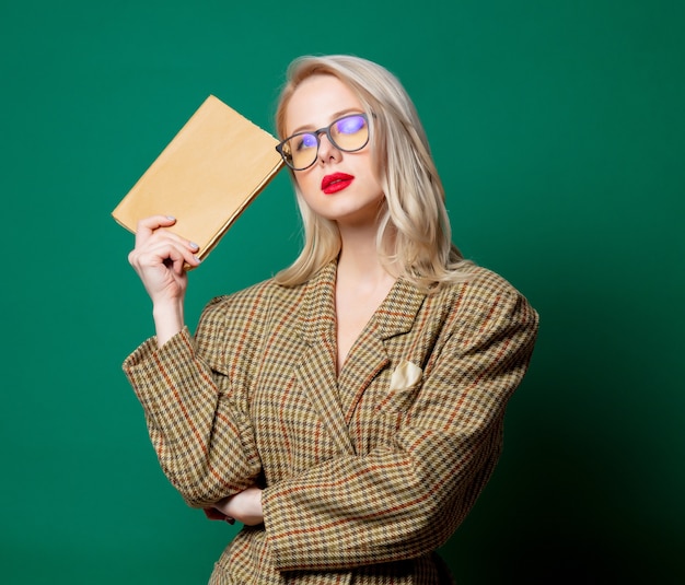 Femme en veste de style britannique avec livre sur mur vert