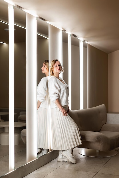 Photo une femme en vêtements blancs se tient appuyée contre un miroir dans la pièce.