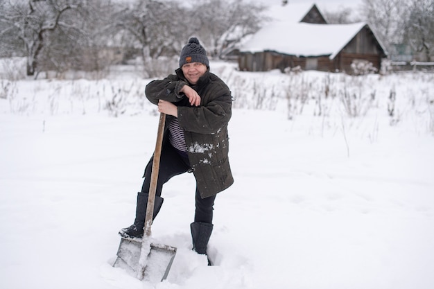 Femme en vêtements chauds avec une pelle enlève la neige de la cour