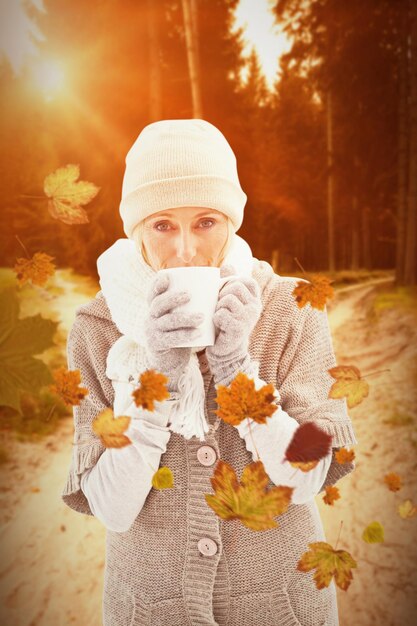 Femme en vêtements chauds tenant des tasses contre la scène d'automne