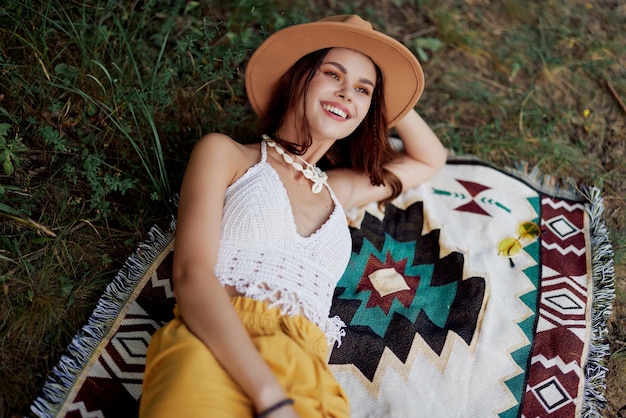 Une femme en vêtements écologiques dans un look hippie est allongée sur un plaid coloré en souriant et en regardant un coucher de soleil d'automne dans la nature dans le parc Style de vie sur un voyage d'harmonie avec le monde