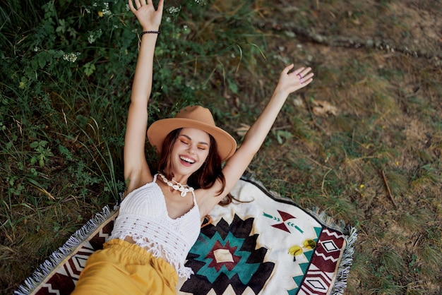 Une femme en vêtements écologiques dans un look hippie est allongée sur un plaid coloré en souriant et en regardant un coucher de soleil d'automne dans la nature dans le parc Style de vie sur un voyage d'harmonie avec le monde