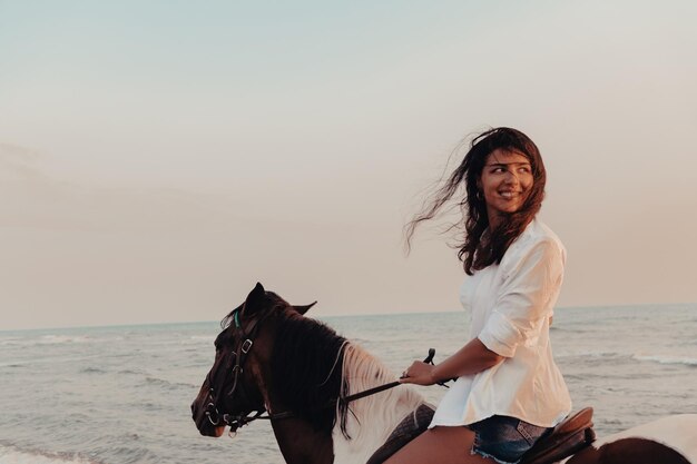 Une femme en vêtements d'été aime monter à cheval sur une belle plage de sable au coucher du soleil. Mise au point sélective. Photo de haute qualité