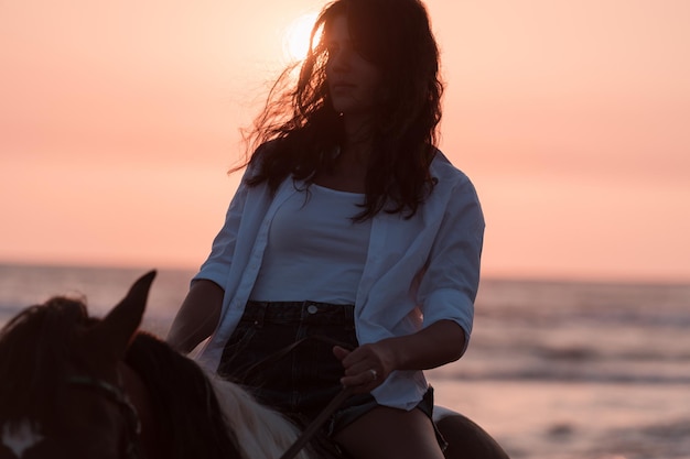 Femme en vêtements d'été aime monter à cheval sur une belle plage de sable au coucher du soleil mise au point sélective