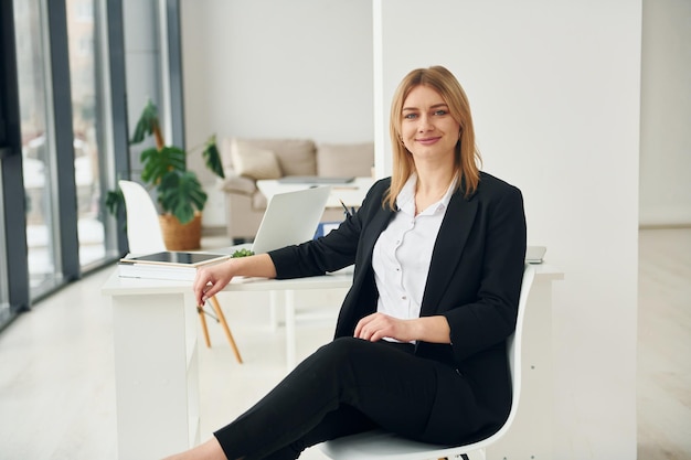 Une femme en vêtements formels est assise sur la chaise à l'intérieur dans le bureau moderne pendant la journée