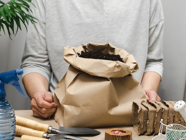 Une femme en vêtements gris tient un sac de terre pour planter des graines dans des gobelets en papier Passe-temps et loisirs