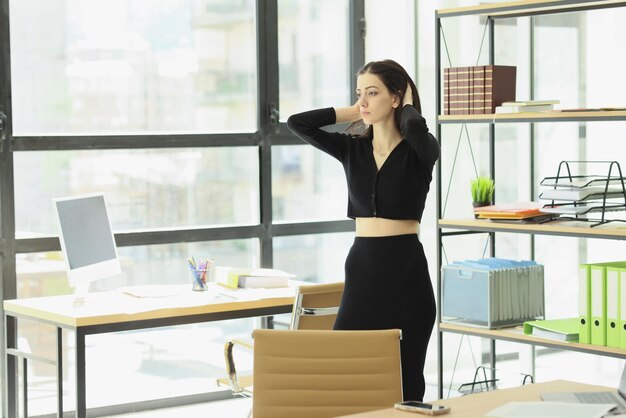 Une femme en vêtements noirs ajuste ses cheveux en traversant son bureau