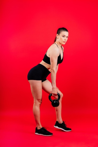 Femme en vêtements de sport faisant un entraînement crossfit avec une cloche de bouilloire sur un fond rouge jaune foncé