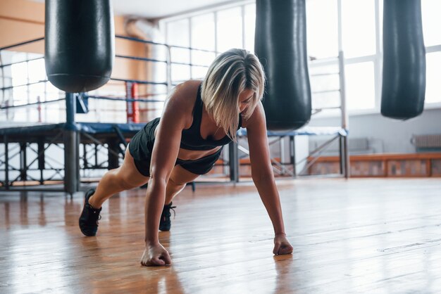 Femme en vêtements de sport noirs ont un exercice de planche sur le sol de la salle de gym.