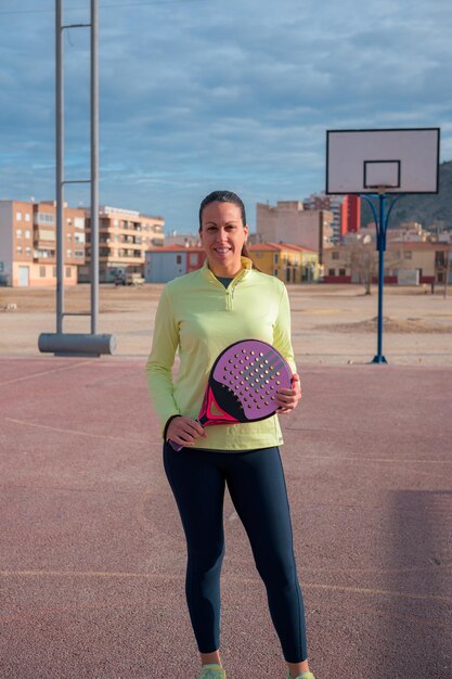 Une femme en vêtements de sport avec une raquette de tennis regarde la caméra
