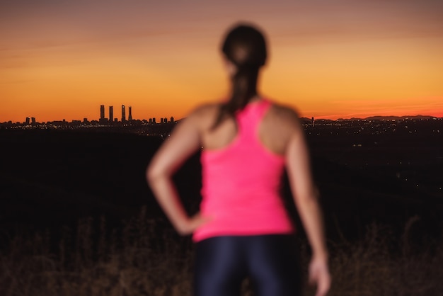 Femme sur les vêtements de sport en regardant le coucher du soleil sur les toits de la ville. L&#39;accent est mis sur le fond.