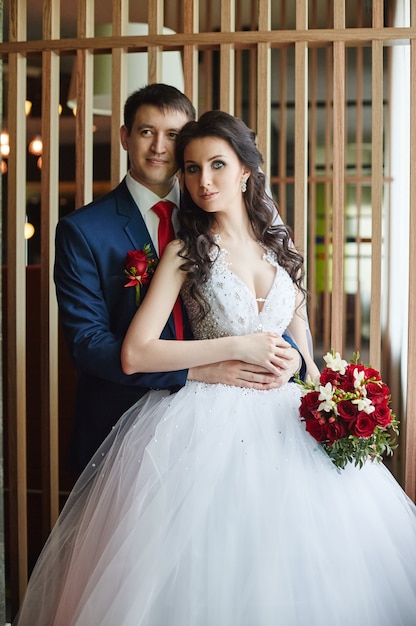 Femme vêtue d'une belle robe blanche et homme vêtu d'un costume bleu se serrant près de la fenêtre. Couple amoureux et affectueux