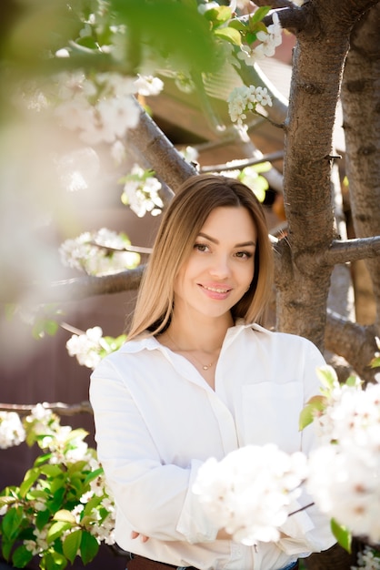 Une femme vêtue d'une chemise blanche et d'un jean dans un jardin printanier.