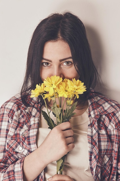 femme vêtue d'une chemise à manches longues à carreaux sentant un bouquet de fleurs jaunes