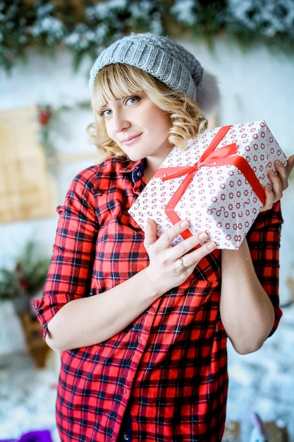 Une femme vêtue d'une chemise de Noël rouge et d'un chapeau sur la tête tient un cadeau de Noël.