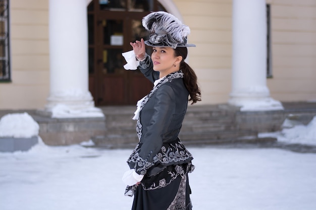 Une femme vêtue comme une noble du 19e siècle se tient près d'un vieux manoir.hiver russe