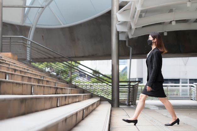 Une femme vêtue d'un costume noir et d'une jupe, elle monte les escaliers.