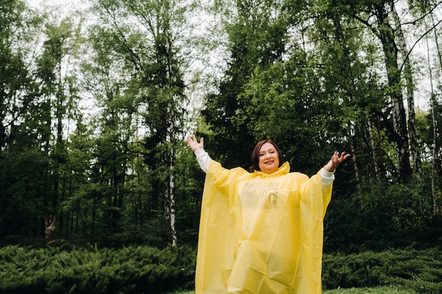 Une femme vêtue d'un imperméable jaune montre des émotions dans le parc en été après la pluie.